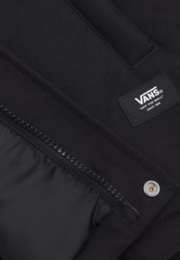 Zwarte stoffen etui met ritssluiting, voorzien van een Vans-label. Het materiaal heeft een gladde textuur met subtiele naden en een metalen drukknop.