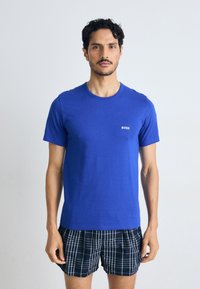 T-shirt de algodão azul de mangas curtas com decote redondo e logotipo branco "BOSS" no lado esquerdo do peito, combinado com calções xadrez azul-escuros.