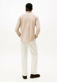 Lys beige langærmet skjorte med buet kant, parret med off-white bukser og mørkebrune sko, set fra ryggen.