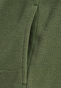 Olijfgroen fleece stoftextuur met een zachte, geborstelde afwerking; heeft een naad met een subtiele splitdetail, wat de functionaliteit vergroot.