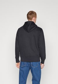 Felpa nera con cappuccio regolabile, maniche lunghe e polsini a costine, abbinata a jeans azzurri chiari. Tessuto morbido, design minimalista.