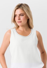 Top sans manches blanc avec un col rond et des bordures argentées. Tissu lisse avec un léger éclat et coupe décontractée. Pas de motifs ni d'accents.