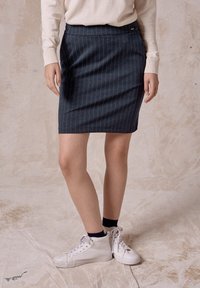 Dunkelblaue Jeansrock mit Nadelstreifen und tailliertem Schnitt. Kombiniert mit weißen High-Top-Sneakern und einem cremefarbenen Pullover.