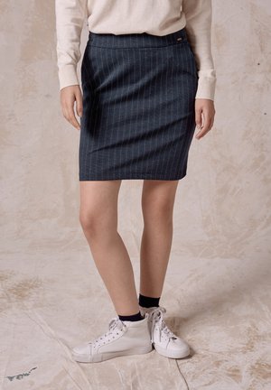 Mörkblå denimkjol med smala ränder och en åtsittande design. Kombinerad med vita högformat sneakers och en krämfärgad tröja.