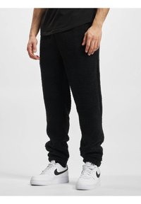 Sorte fleece joggebukser med strukturert stoff, elastiske mansjetter, og avslappet passform. Brukt med hvite Nike sneakers med svart swoosh.