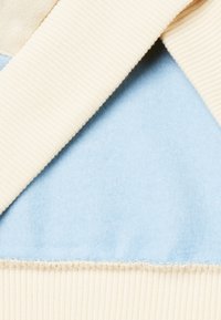 Un tessuto a costine crema si combina con una morbida felpa azzurro chiaro, caratterizzato da una cucitura pulita lungo il bordo, creando un design stratificato e testurizzato.
