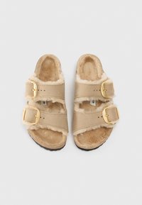 Bežid sandaalid kahe reguleeritava rihmaga, karvase voodriga ja kuldsete haaknuppudega. Pehme tekstuur ja robustne põhi.