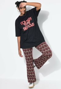 Zwarte oversized t-shirt met rode neontekst "HET IS NICHT ZO SERIEUS," gecombineerd met gestreepte bordeauxrode flared broeken en witte sneakers.