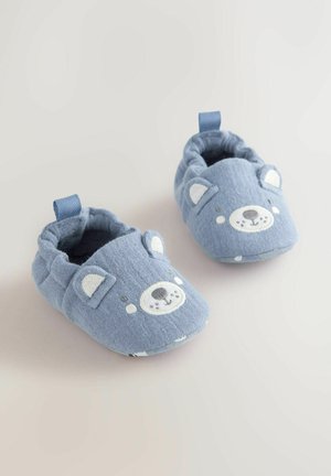 Papuci de casă din material albastru cu design cu fața unui urs, având urechi și nas brodate și deschideri elasticizate pentru a fi ușor de încălțat.