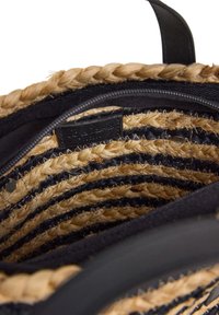 Insidan av en flätad halmhandväska med växelvis svarta och naturliga färgade ränder, svart tygfoder och en liten etikett. Design med öppen topp.