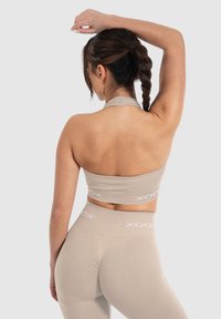 Conjunto de ropa deportiva beige compuesto por un top corto con cuello halter y leggings de tiro alto con textura acanalada y acentos de logo blanco en contraste.