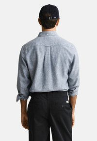 Lichtblauw, knoopsluiting, langemouw shirt met een rugplooien, gedragen met een zwarte broek. Het shirt heeft opgerolde mouwen en een kraag.