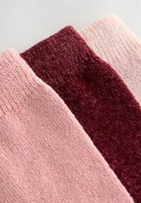 Trys megztos kojinės šviesiai rožinės, burgundiškolinės ir šviesiai bežinės spalvų. Medžiaga atrodo minkšta ir tekstūruota, su banguotais kraštais.