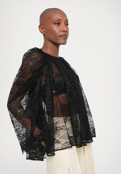 Must Valge pitspluus, millel on läbipaistvad, voolavad varrukad ja kogutud kaelus. Esitleb keerukaid lillemustreid ja kihilist disaini musta pluusi peal.