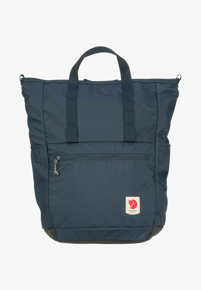 Tummansininen nailoninen kassi, jossa on kaksi yläsangat, vetoketjullinen etutasku ja neliönmuotoinen logopatchi, jossa on punainen kettu alareunassa.