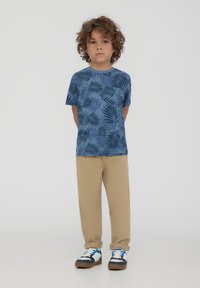 T-shirt azzurro a maniche corte con un motivo di foglie scure, abbinato a pantaloni beige e sneaker colorati. Tessuto morbido e design casual.