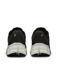 Chaussures de sport noires avec une tige texturée, une semelle intermédiaire blanche contrastante et une semelle extérieure en caoutchouc robuste. Présente un marquage minimal au niveau du talon.