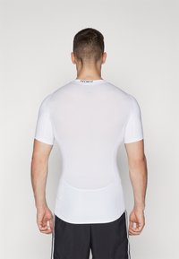 Hvid kortærmet kompressionsskjorte med mesh-struktur og "TECHFIT" label bagpå, tætsiddende design, glat stof.