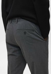 Grijze op maat gemaakte broek met een subtiel ruitpatroon, voorzien van twee achterzakken en een knoopaccent. Gemaakt van een gladde, textuurstof.