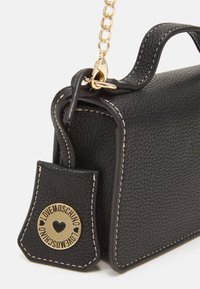 Svart texturerad läderväska med en kedjesnor i guld, guldiga detaljer och logotagg. Har kontrasterande vit sömnad och rektangulär form.