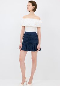 Off-shoulder vit topp med volangärmar, i kombination med en marinblå minikjol med rynk och utsvängd nederkant. Neutrala högklackade skor.