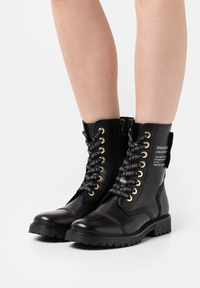 Black leather combat boots with gold hardware and decorative laces featuring printed text. Includes a side zipper and chunky soles for durability.