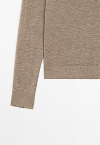 Beżowy sweter dzianinowy z długimi rękawami i ribbowym wykończeniem. Miękka tekstura z delikatnym połączeniem jasnych i ciemnych włókien. Prosty, klasyczny design.