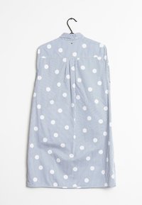 Camisa a rayas azul claro con grandes lunares blancos, con cuello y pliegue en la parte posterior, colgando de un gancho negro.