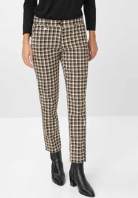 Spodnie w wzór houndstooth w kolorach brązowym, kremowym i czarnym; slim fit z średnim stanem, zestawione z czarnymi botkami za kostkę.