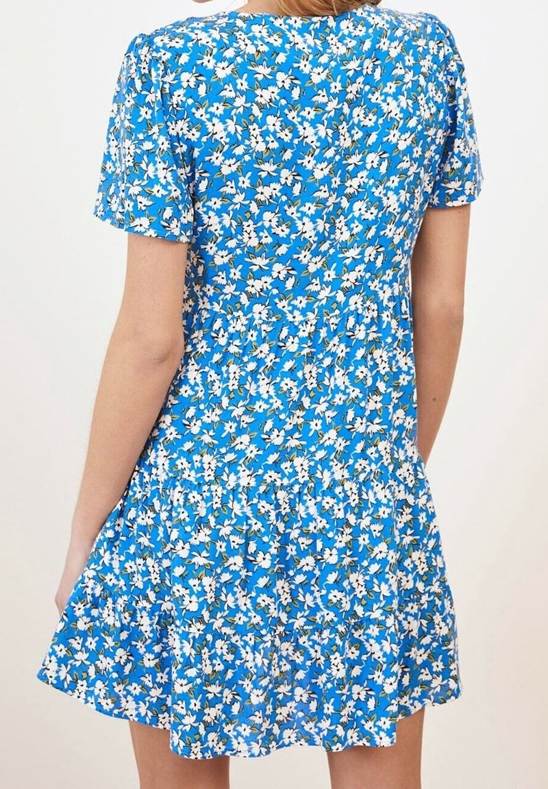 Robe bleue à manches courtes avec imprimé floral blanc portée par une personne vue de dos, se terminant au-dessus des genoux.