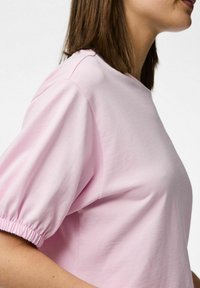 Vaaleanpunainen lyhythihainen t-paita pehmeästä puuvillasta. Ominaisuuksiin kuuluu pyöreä kaula-aukko ja rypytetyt yksityiskohdat hihansuiden kohdalla. Sujuva pinta.