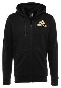 Sudadera negra con cremallera y cordones, con el logo dorado de Adidas en el lado izquierdo del pecho, que cuenta con bolsillos frontales y puños y dobladillo acanalados.