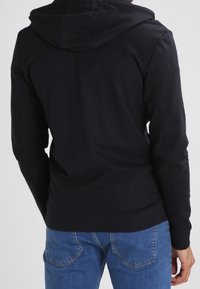 Sweat à capuche noir en tissu mélangé coton, doté d'une capuche avec cordon de serrage, de manches longues et d'un ourlet côtelé, associé à un jean bleu clair.