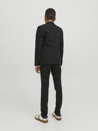 Zwarte colbert en broek met een slim fit, gecombineerd met witte sneakers. Het colbert heeft een notch-kraag en rugventilatie.