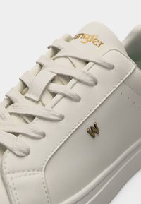 Λευκό δερμάτινο αθλητικό παπούτσι με λευκά κορδόνια, χρυσό λογότυπο "Wrangler" στη γλώσσα και μικρό χρυσό έμβλημα "W" στην πλευρική επιφάνεια.