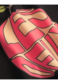 Svart stoff med en stor, stilisert grafikk som har rosa og beige bokstaver. Designet inkluderer buede linjer og aksenter, noe som fremhever teksturen.
