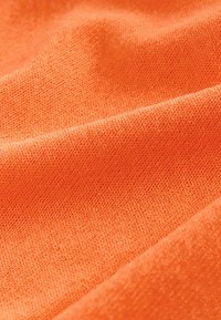 Gros plan sur un tissu tricoté doux de couleur orange avec une texture fine visible et des plis délicats.