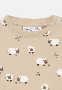 Bežna bombažna srajca z vzorcem risanih ovac v beli in rjavi barvi, s črnimi tačkami, okroglimi obrazi in mehkobo tkanine.