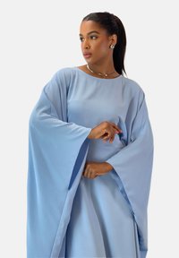 Hellblauer Kaftan mit weiten Ärmeln, glatter Textur und lockerem Schnitt. Verfügt über einen runden Ausschnitt und subtile Seitenschlitze.