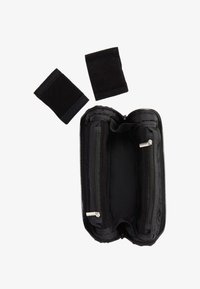 Bolsa negra con cremallera abierta que muestra dos compartimentos interiores, junto a dos muñequeras de tela negra separadas sobre un fondo blanco.