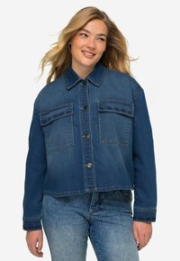 Giacca di jeans blu con un design leggermente accorciato, due tasche sul petto e cuciture di accentuazione blu scuro sulle tasche e sui polsini.
