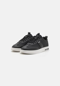 Fekete sneaker sima bőrből és hálós részletekből. Fehér gumitalppal és fekete fűzőkkel rendelkezik. Az oldalán egy kis logó díszítés található.