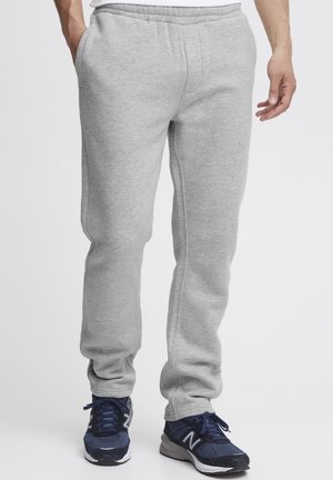 Gray sweatpants made from soft fabric, featuring an elastic waistband, side pockets, and tapering cuffs. Worn with navy athletic shoes.