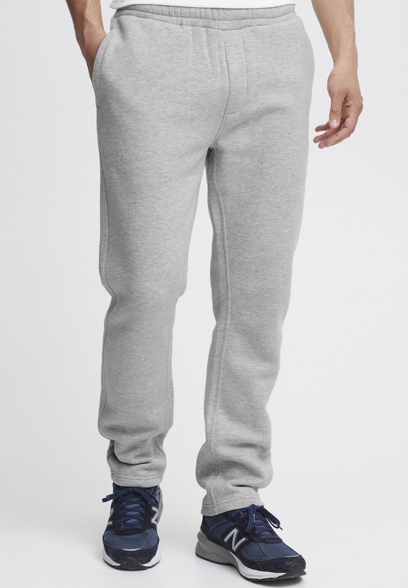 Gray sweatpants made from soft fabric, featuring an elastic waistband, side pockets, and tapering cuffs. Worn with navy athletic shoes.