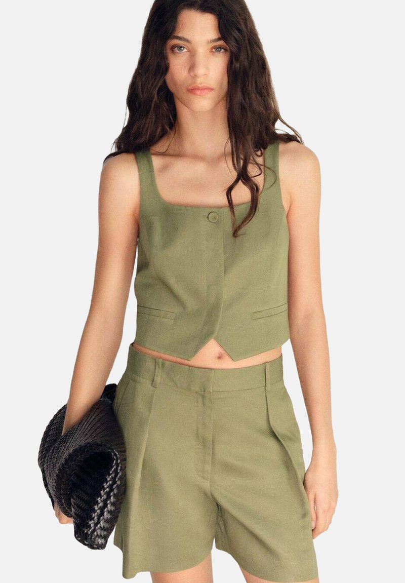 Olivově zelený cropped top s čtvercovým výstřihem a zapínáním na knoflíky, v kombinaci s odpovídajícími šortkami s vysokým pasem. Černá pletená kabelka.
