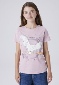 Lichtroze katoenen t-shirt met een uil grafiek, een toverstok en de tekst "Welkom op Zweinstein". Korte mouwen en een klassiek ronde hals ontwerp.