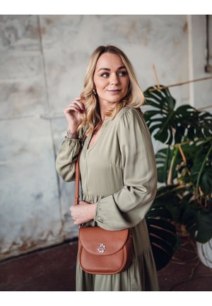 Braune Leder-Crossbody-Tasche mit Klappenverschluss, runder Form und geprägtem Logo. Weiches olivgrünes Kleid aus Stoff mit puffärmel.
