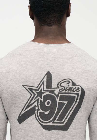 Γκρι πλεκτό πουλόβερ με μεγάλο μαύρο γραφικό σε σχήμα αστέρι και τη φράση «Since 97» καθώς και τον αριθμό «97» με έντονη γραμματοσειρά στην πλάτη.