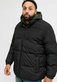 Musta toppatakki, jossa on vetoketjullinen etukappale, korkea kaulus ja joustavat hihansuut. Takissa on teksturoitu, tikattu kuvio ja sivutaskut.