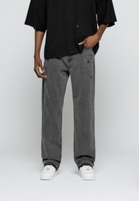 Camiseta negra holgada y vaqueros de mezclilla gris. Los vaqueros presentan detalles desgastados. Combinados con zapatillas blancas. Diseño sencillo, estilo casual.